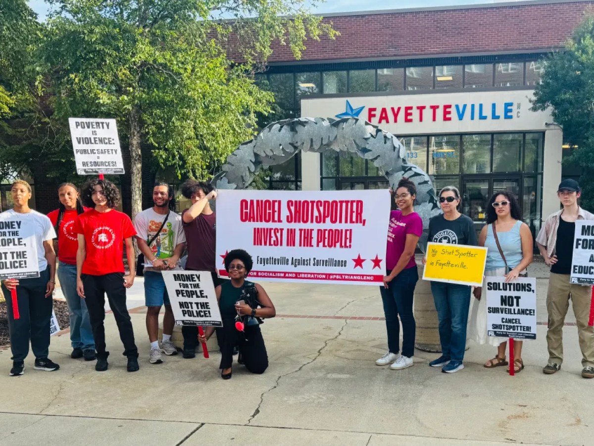 A group of people holding signs stand outside a building