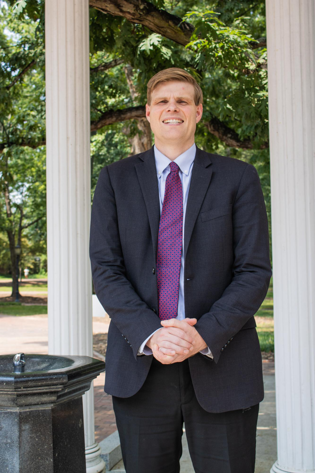 A man in a suit stands in front of UNC-CH's Old Well